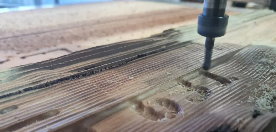 The router cutting lettering into hardwood, chips coming off the bit